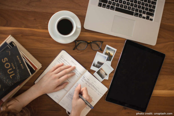 Image of a person taking notes at a table with a laptop